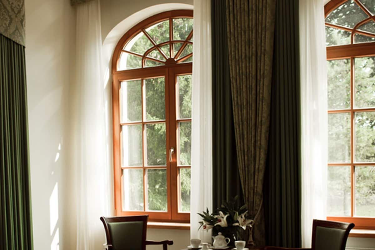 A room with a bed, two chairs, a small table with a teapot and cups, and a window with curtains.
