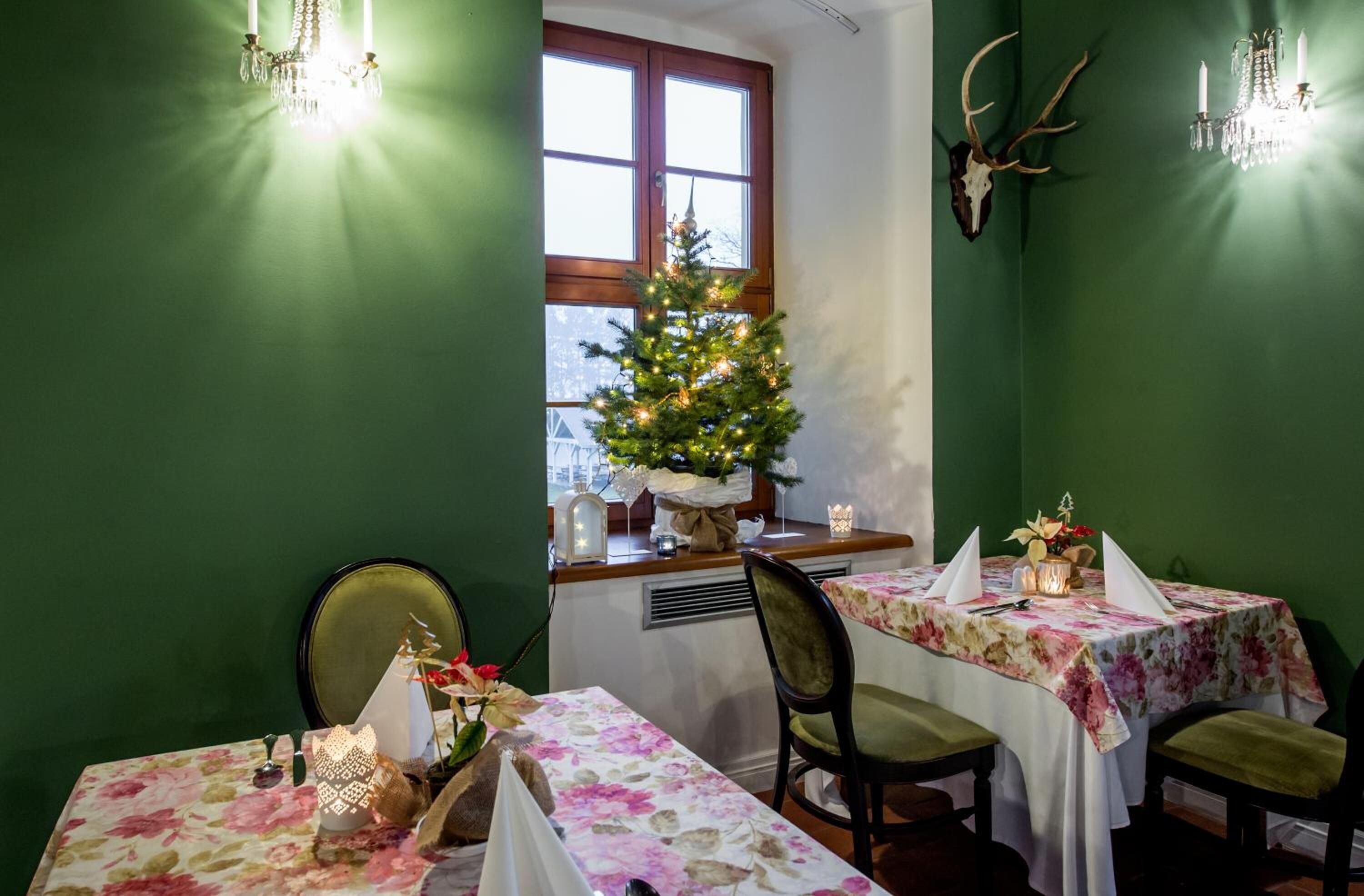 Un comedor con paredes verdes, un árbol de Navidad, candelabros y decoraciones de cuernos de ciervo.