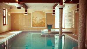A large indoor swimming pool with a central fountain, surrounded by stone pillars and a mural on the wall. - Pałac w Rymaniu (Ryman)
