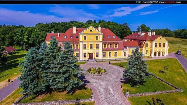 A large, yellow building with a red roof, surrounded by trees and a gravel driveway. - Pałac w Rymaniu (Ryman)