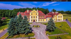 A large, yellow building with a red roof, surrounded by trees and a gravel driveway. - Pałac w Rymaniu (Ryman)