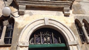 Fachada de edificio con un arco de piedra, una cruz sobre el arco y una reja metálica.