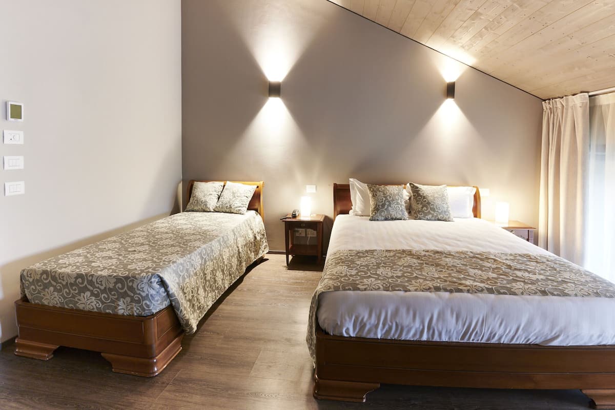 A hotel room with two single beds, wooden headboards, a nightstand, and a wall-mounted light fixture.