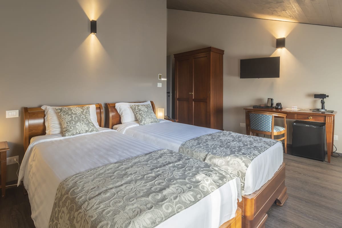 A hotel room with a double bed, bedside tables, a desk with a chair, a wardrobe, and a TV mounted on the wall.