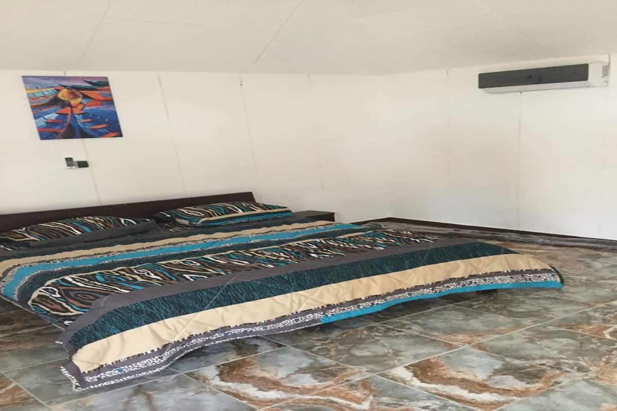 Un dormitorio con cama, colcha estampada, un cuadro en la pared y suelo de baldosas.