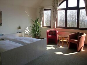 Une chambre avec un grand lit, une chaise, une petite table et une plante en pot.
