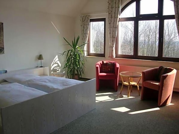 Une chambre avec un grand lit, une chaise, une petite table et une plante en pot.
