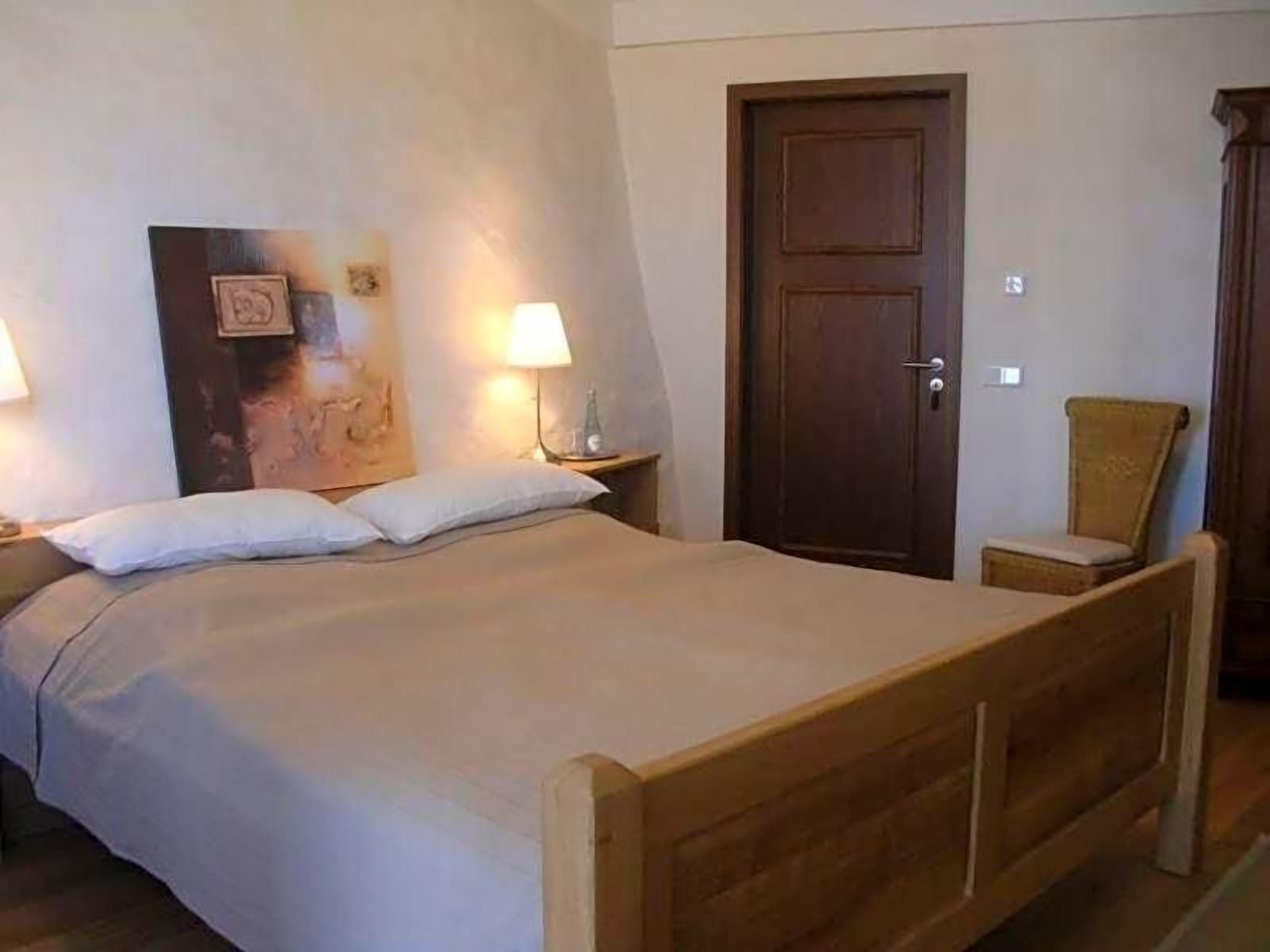 A bedroom with a wooden bed, two bedside lamps, a door, and a chair.