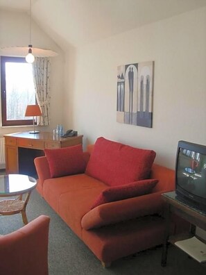 A room with a sofa, a television, a desk, and a chair.