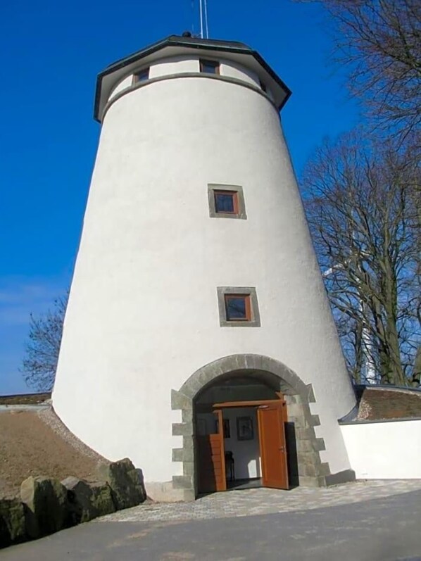 A cylindrical lighthouse with a door and windows, set against a clear sky.