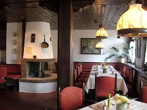 L’intérieur d’un restaurant présente une longue table à manger, des chaises à revêtement rouge, une cheminée en briques et des lampes suspendues.