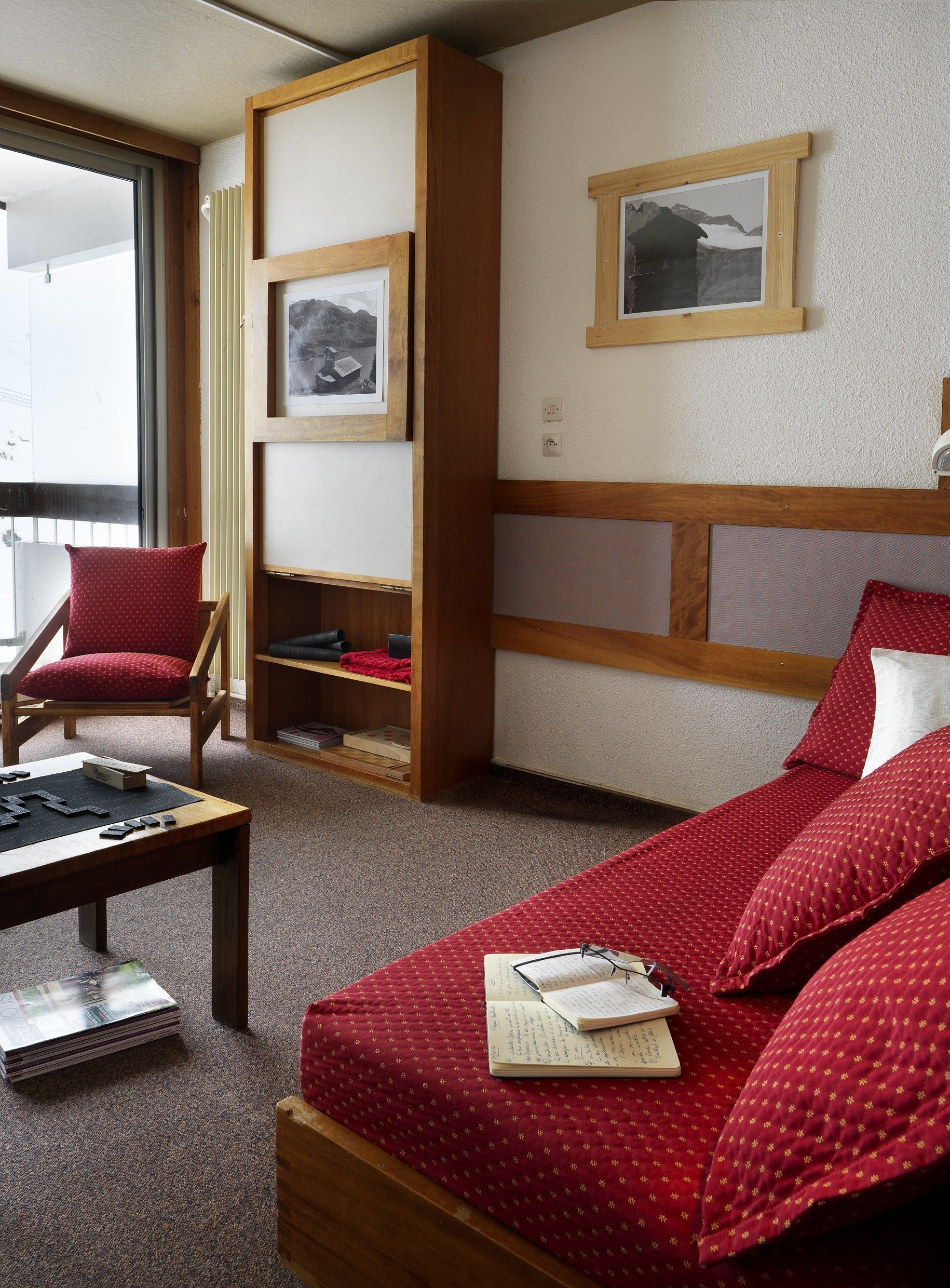 Ein Hotelzimmer mit einem Bett, einem Schreibtisch mit einem Gesellschaftsspiel, einem Sessel und einem Bücherregal.