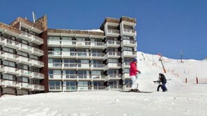 Een hotel met meerdere verdiepingen en balkons, gelegen in een besneeuwd gebied met een skipiste op de achtergrond.