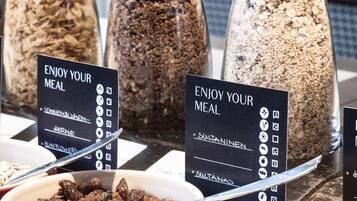 Un bufé con diversas opciones de comida en recipientes transparentes, cada uno con una etiqueta que indica el tipo de alimento.
