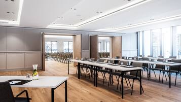 A modern conference room with long tables, chairs, and a large window providing natural light.