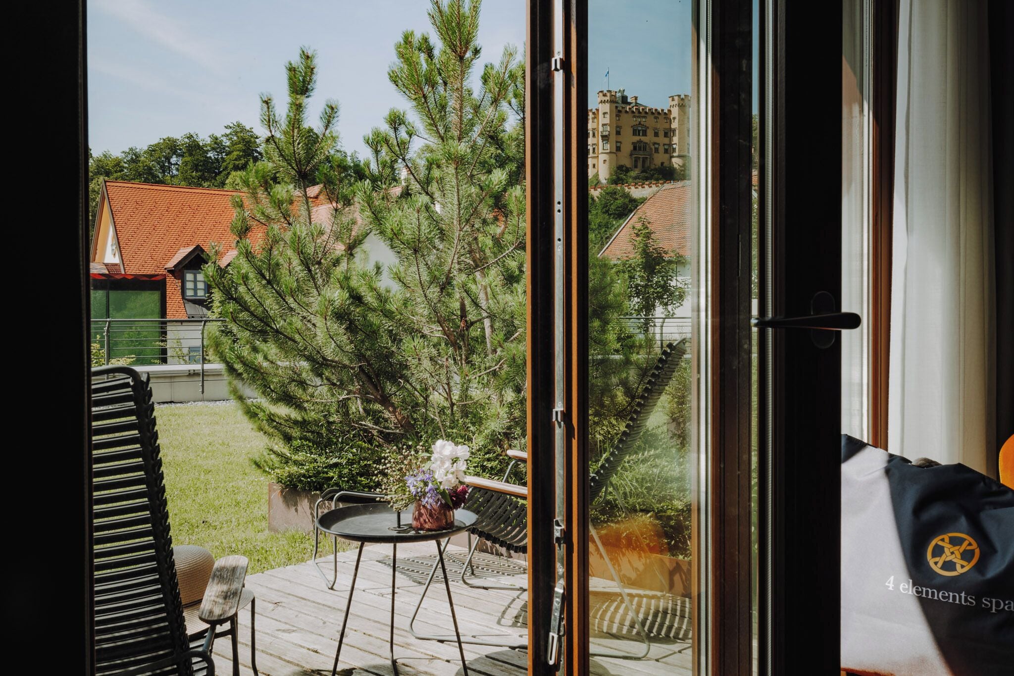 Vista da una stanza con porta scorrevole su un terrazzo esterno. Il terrazzo presenta un tavolo con sedie e un'amaca.