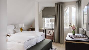 A bedroom with a bed, bedside table, lamp, chair, desk, and a window with curtains.