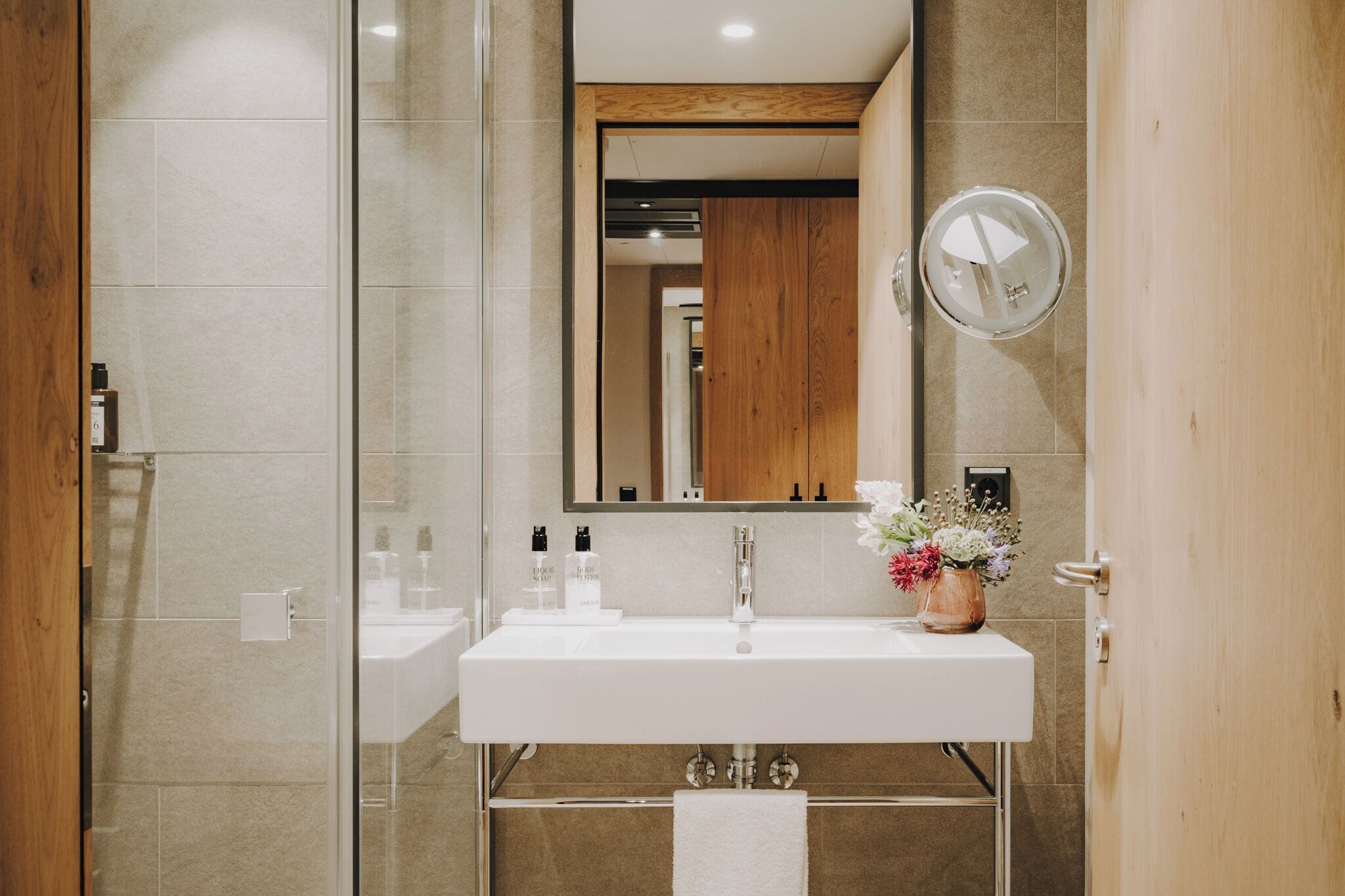 Un baño moderno con lavamanos blanco, espejo y detalles de madera.