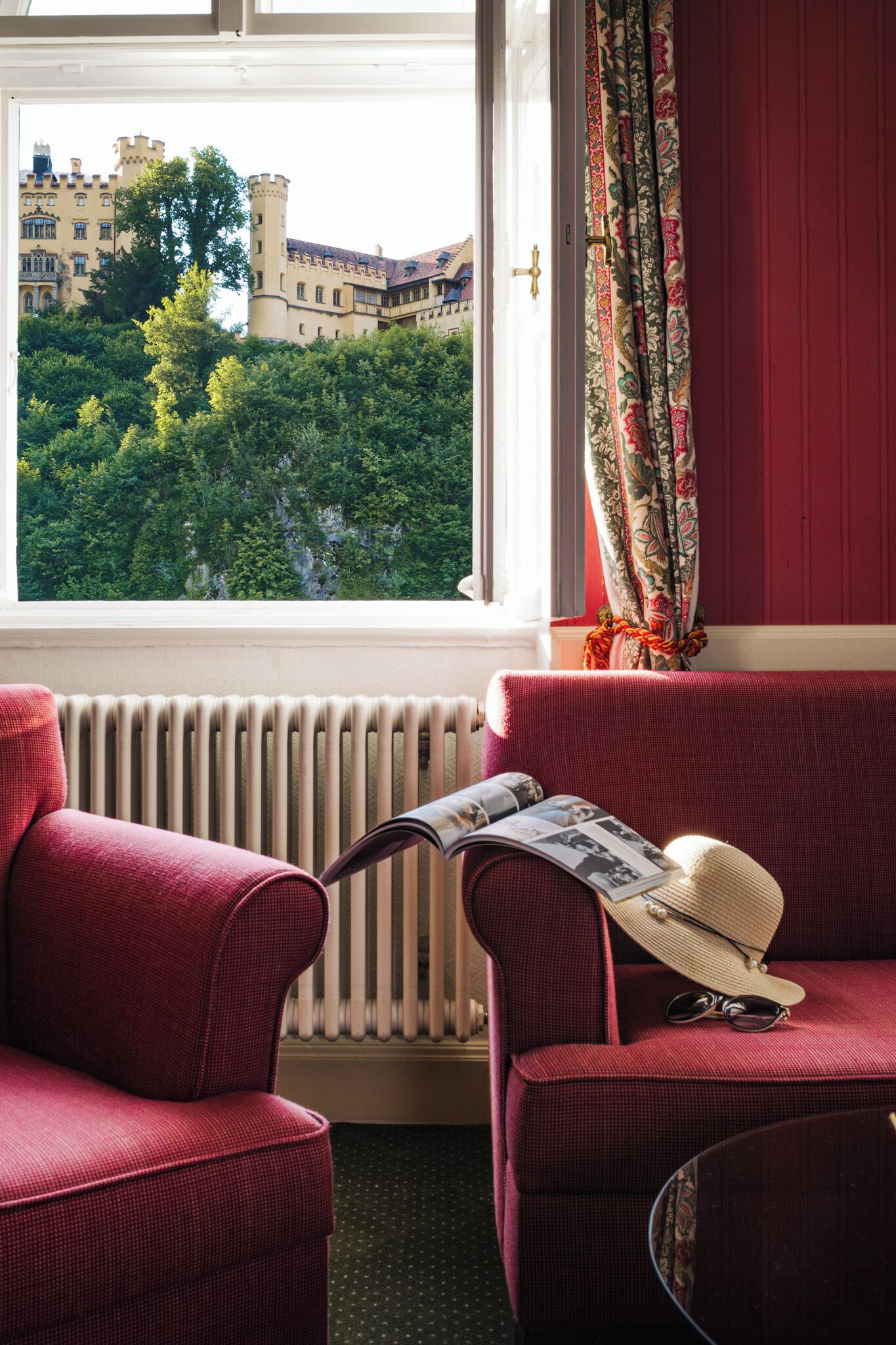 Ein Zimmer mit großem Fenster, Heizkörper, rotem Sofa und einem Sessel.