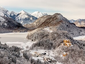 Un paisaje montañoso nevado con un lago, un edificio parecido a un castillo y un conjunto de casas.
