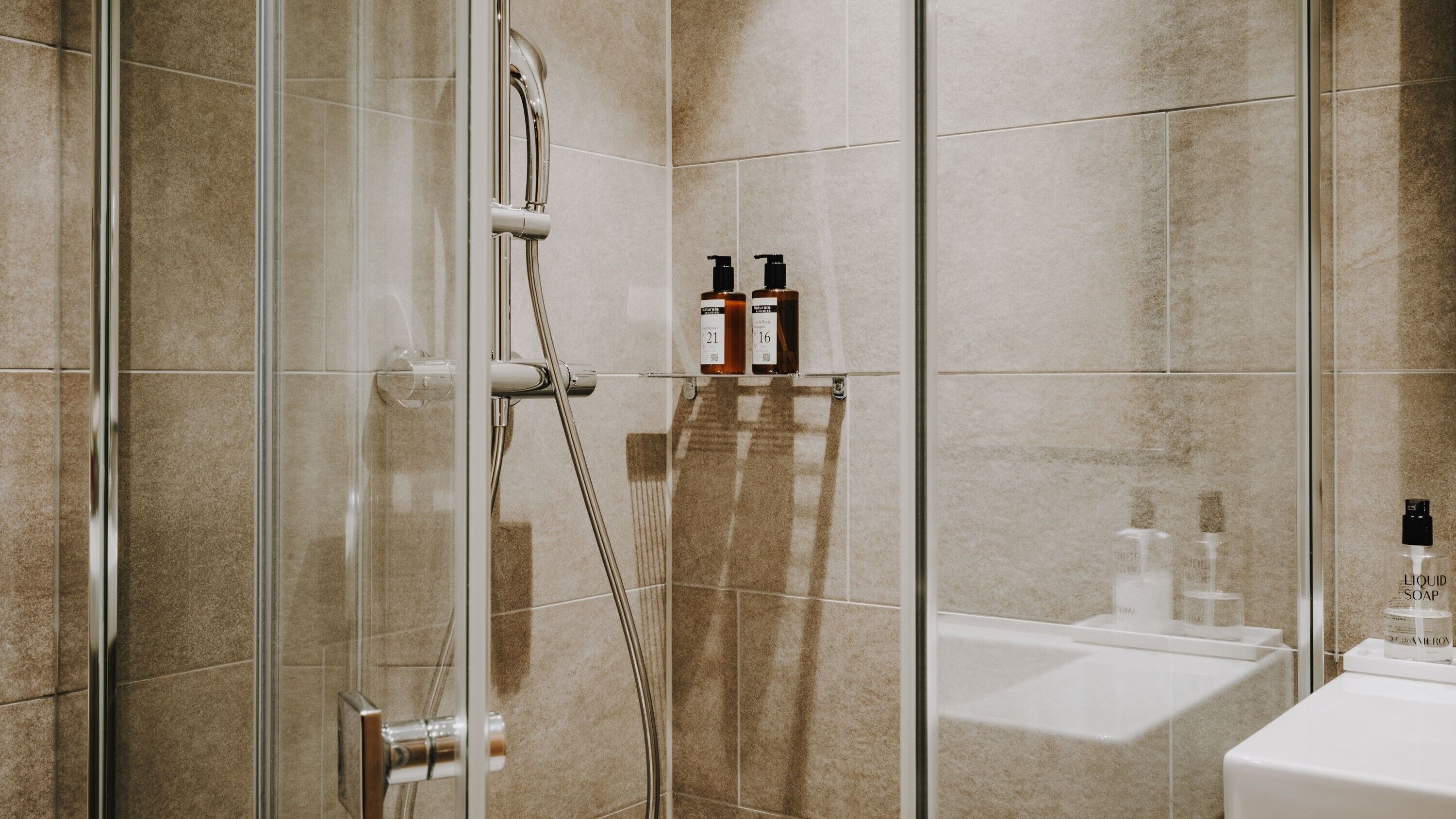 Un bagno moderno con doccia vetrata, lavandino bianco e articoli da toilette su un ripiano.