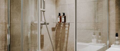A modern bathroom with a glass-enclosed shower, a white sink, and toiletries on a shelf.