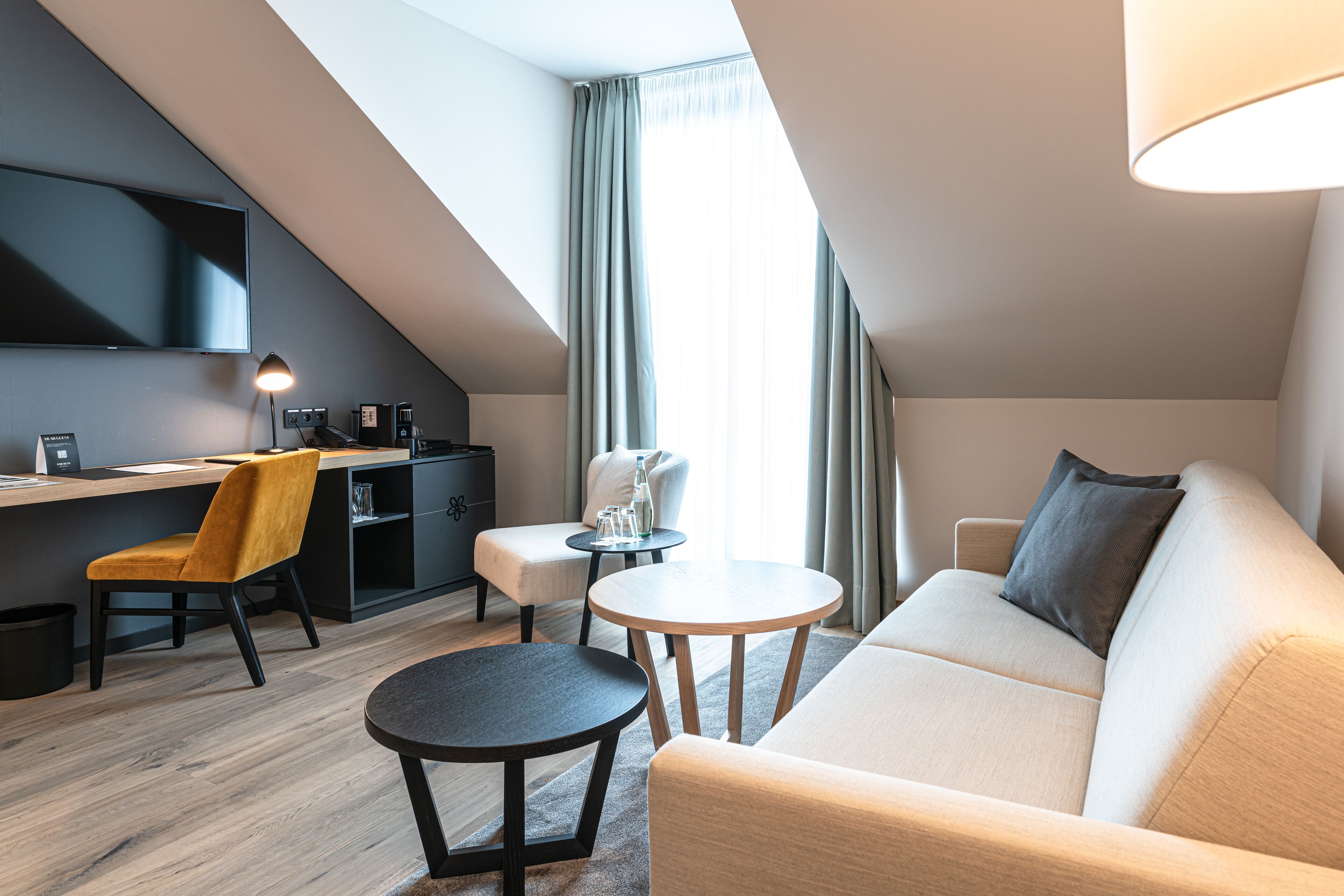 Una habitación moderna y bien iluminada con un sofá, dos sillones, una mesita, un escritorio con una computadora y un televisor.