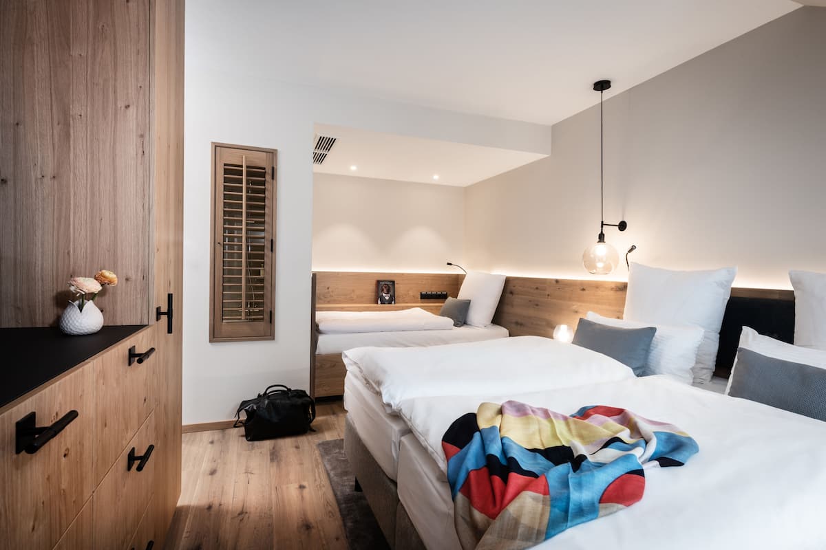 A modern bedroom with two beds, wooden wardrobe, and a window with blinds.
