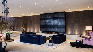 A modern living room with a large fireplace, dark wood paneling, and a staircase with a wooden railing.