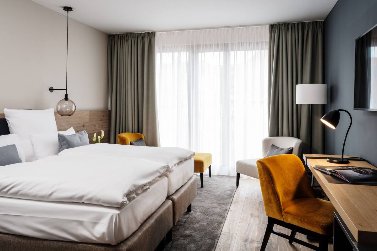 A hotel room with a large bed, a desk, a chair, a lamp, and a TV.