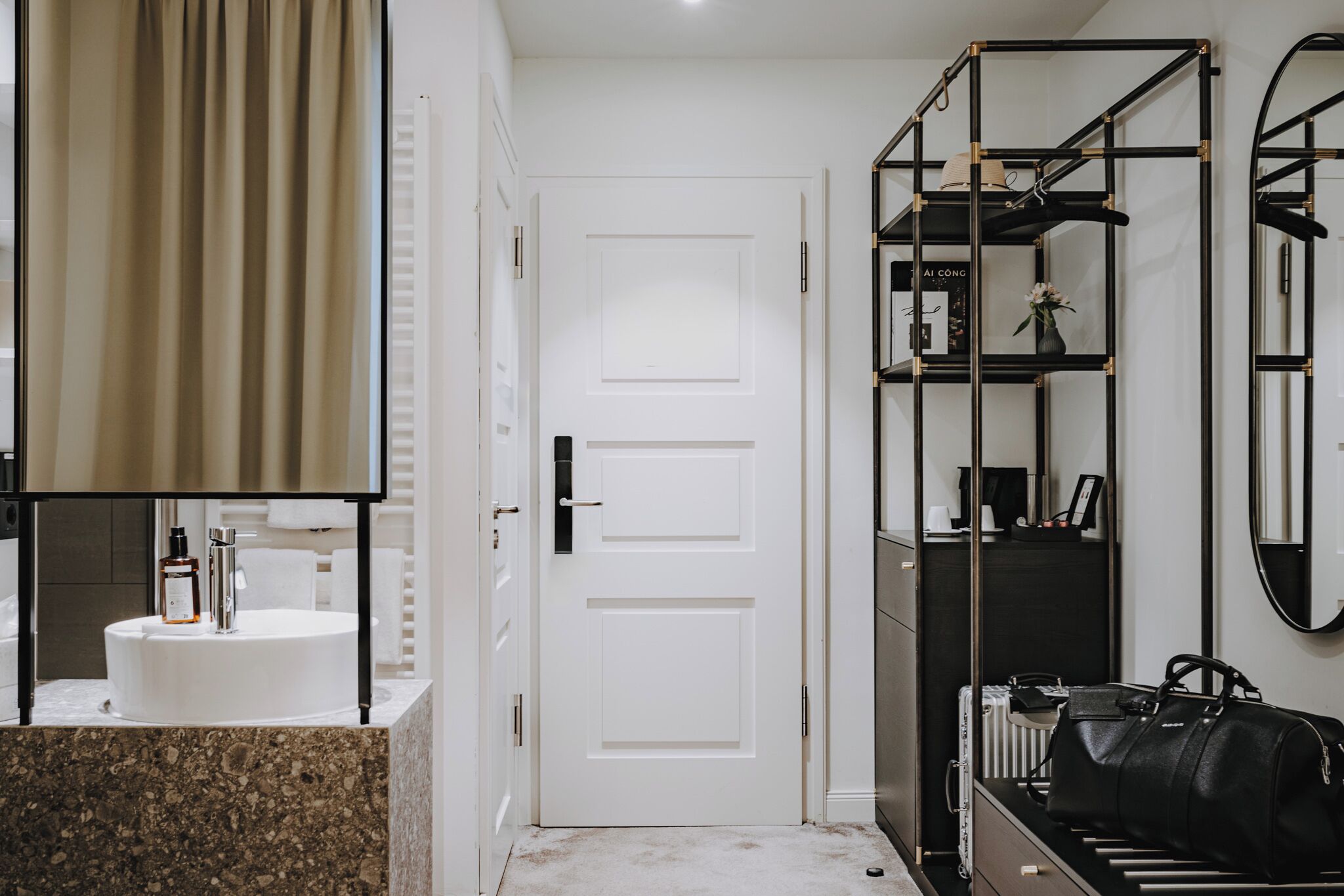 A modern bathroom with a white sink, a mirror, and a black storage unit with shelves.