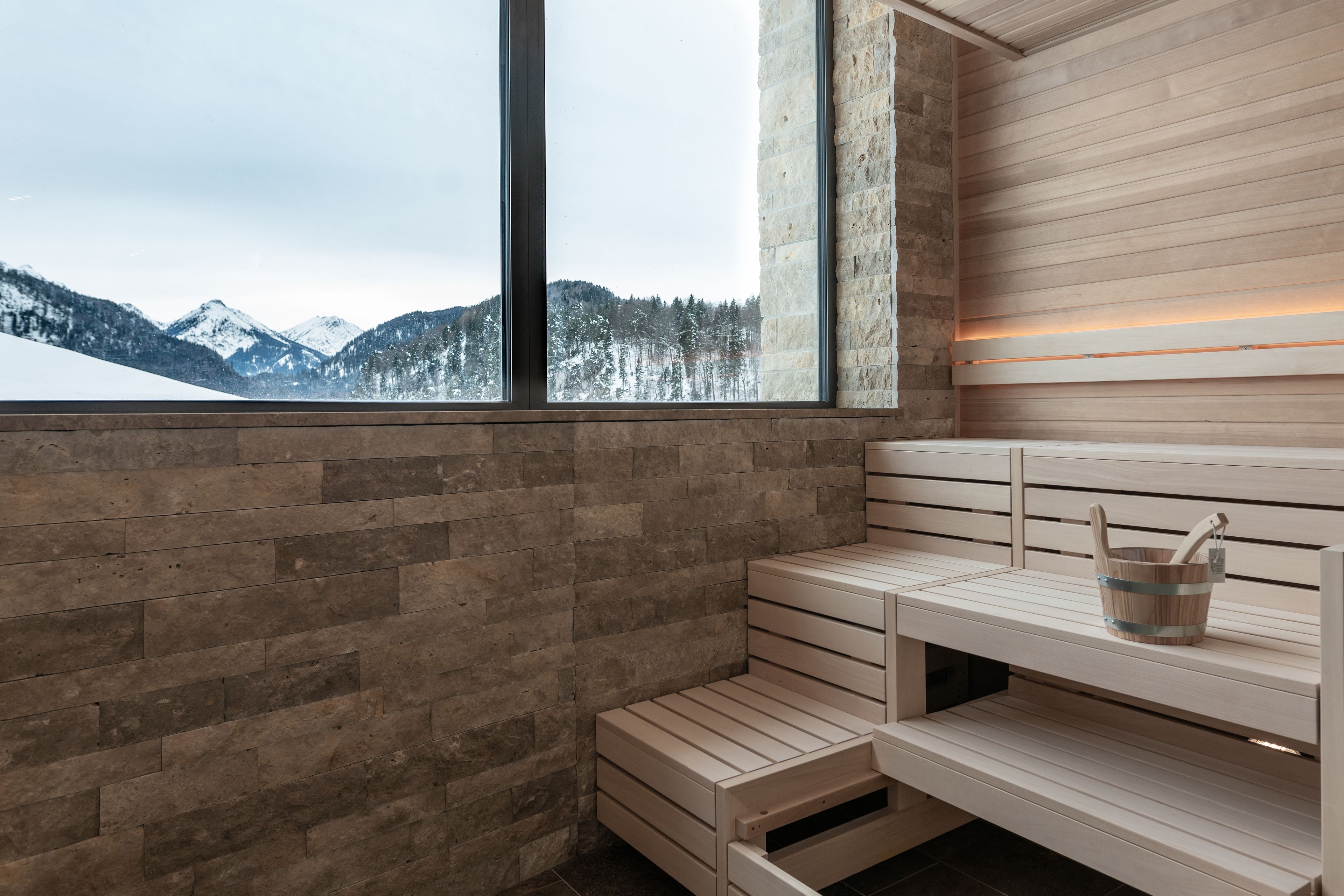 Un sauna avec des bancs en bois, un mur en pierre et une grande fenêtre donnant sur une vue imprenable sur les montagnes.