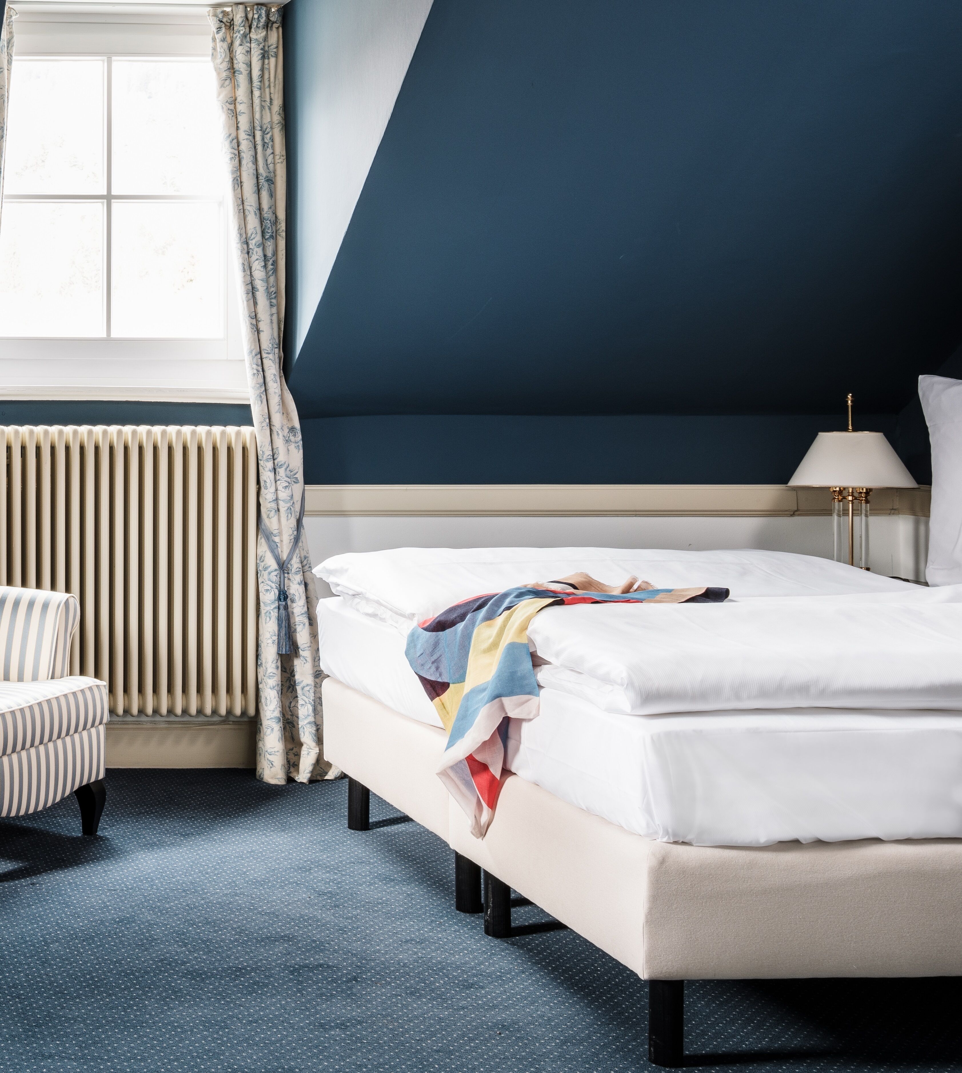 A neatly arranged bedroom with a bed, a chair, a lamp, and a radiator.