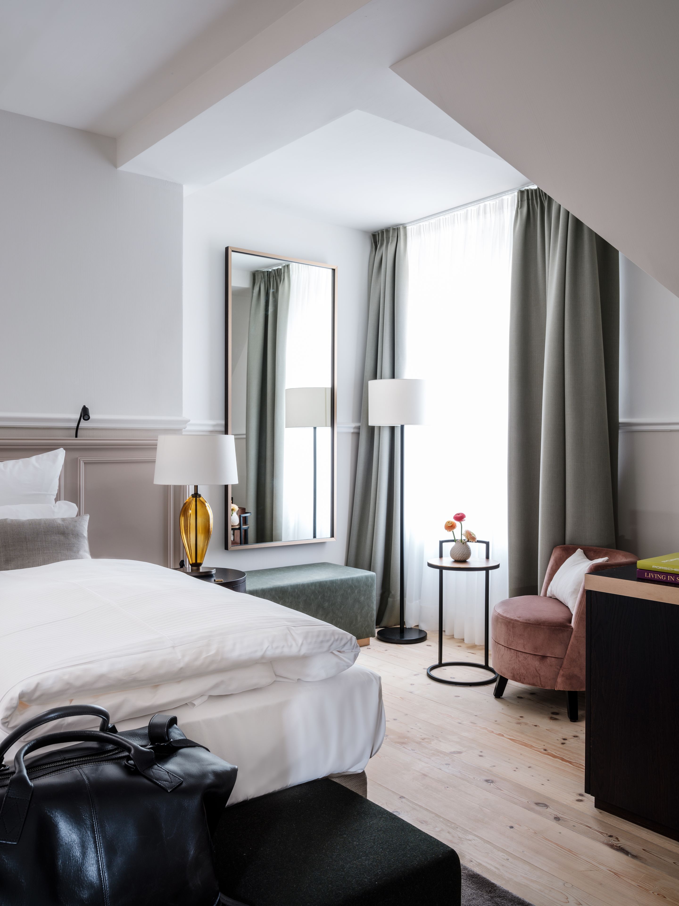 Une chambre d’hôtel moderne avec un grand lit, un bureau, une chaise, une petite table avec une lampe et un grand miroir.