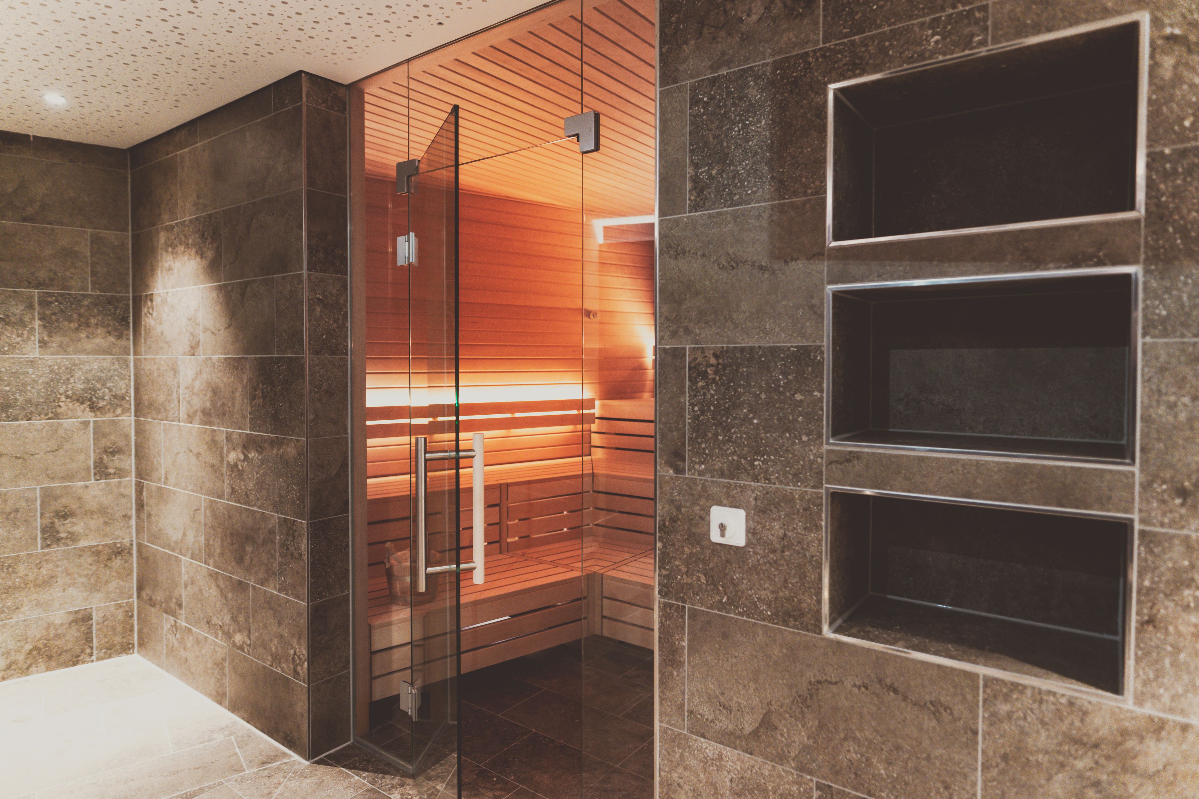 A modern bathroom with a glass-enclosed shower, tiled walls, and built-in shelves.