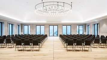 Un salón amplio con filas de sillas orientadas hacia un escenario central, ventanas grandes y una lámpara moderna.