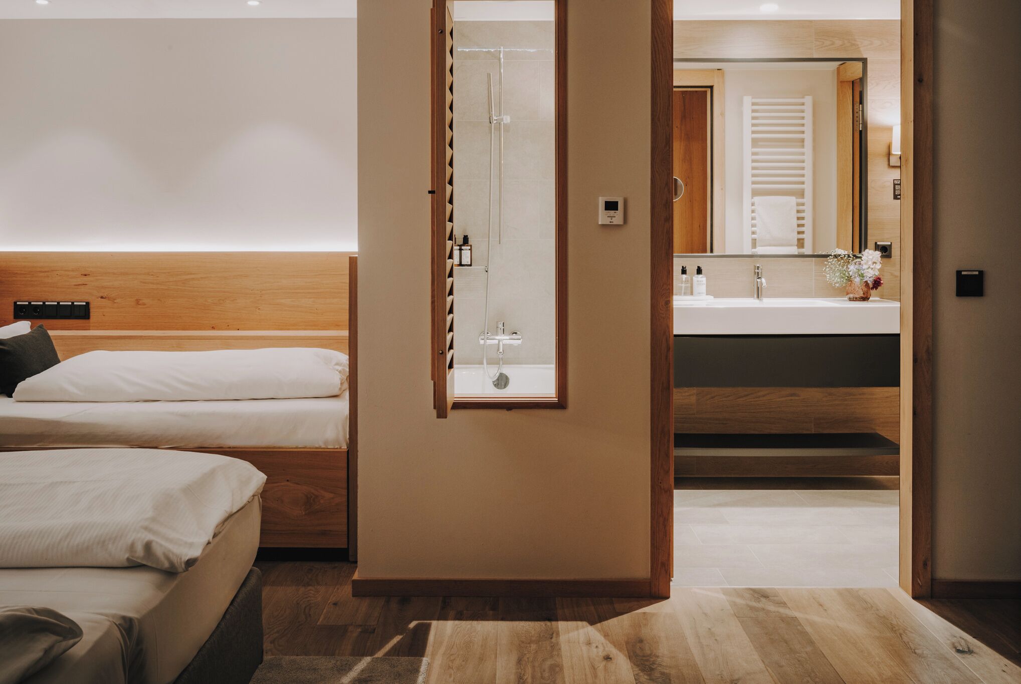 Una habitación de hotel moderna con cabecera de madera, ducha, un espejo grande y un baño con lavamanos e inodoro.