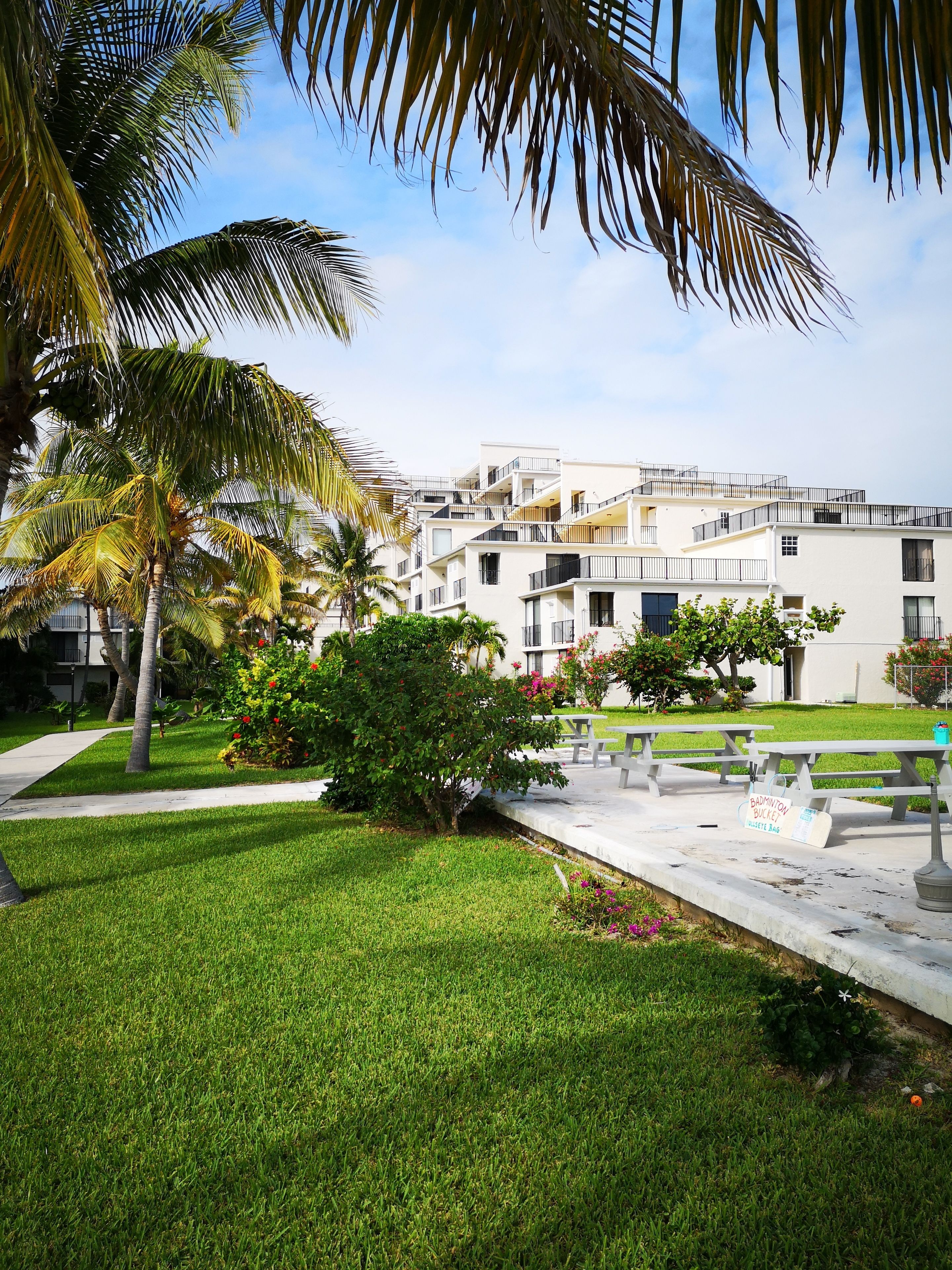 A modern building with multiple balconies, surrounded by well-maintained lawns and palm trees.