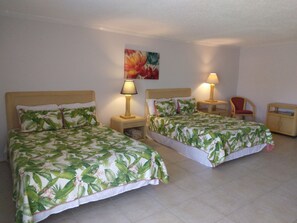 A hotel room with two single beds, each with a nightstand and a lamp. There is a chair and a small wooden cabinet in the room. - Coral Beach Hotel and Condominiums (Freeport)