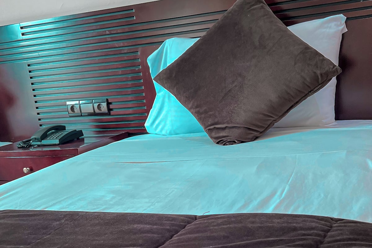 Ein ordentlich bezogenes Bett mit einer braunen Decke, einem türkisfarbenen Kissen und einem weiteren braunen Kissen an einem hölzernen Kopfteil.