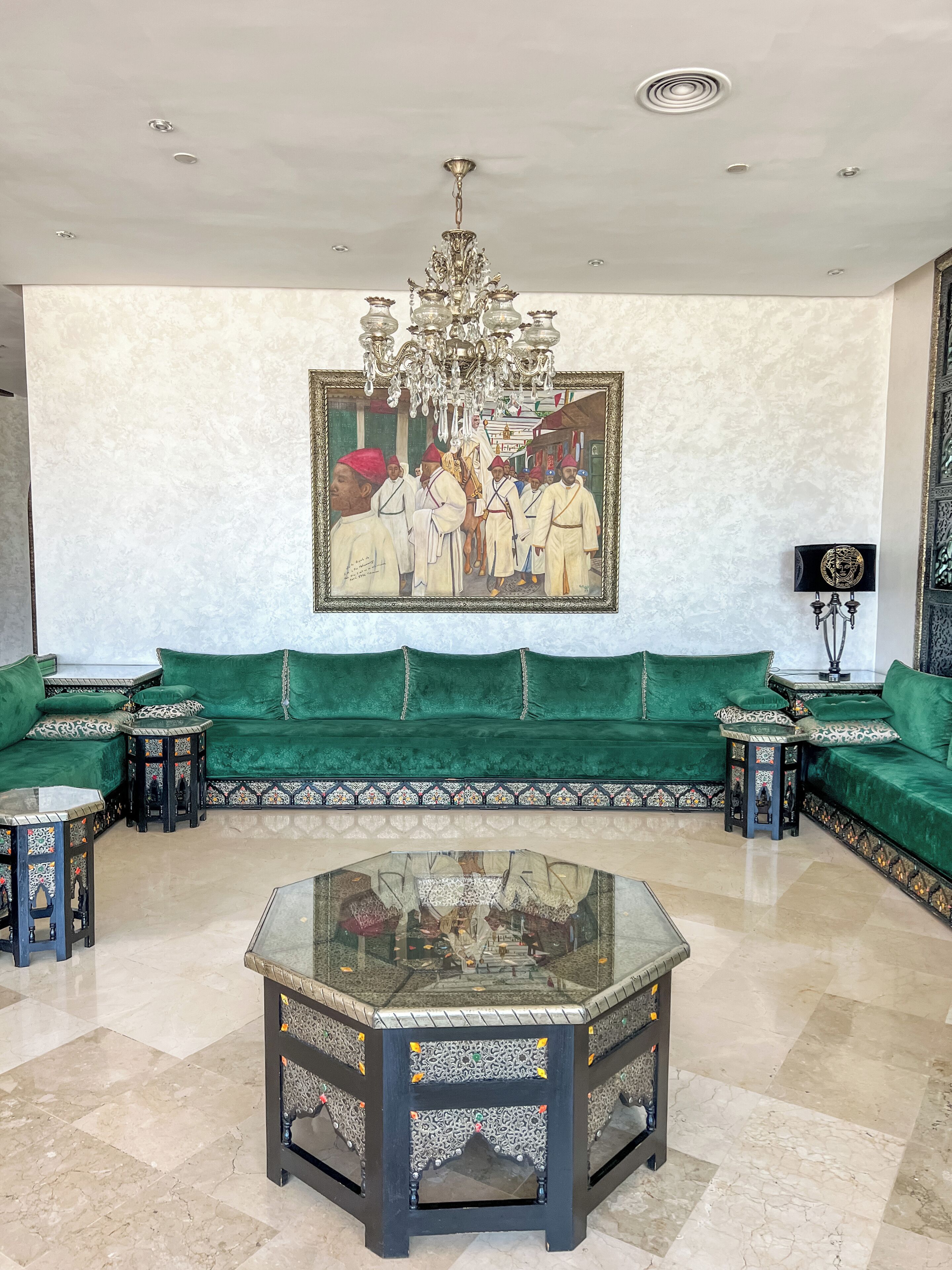 A spacious room with a green sofa set, a large ornate chandelier, and a traditional painting on the wall.