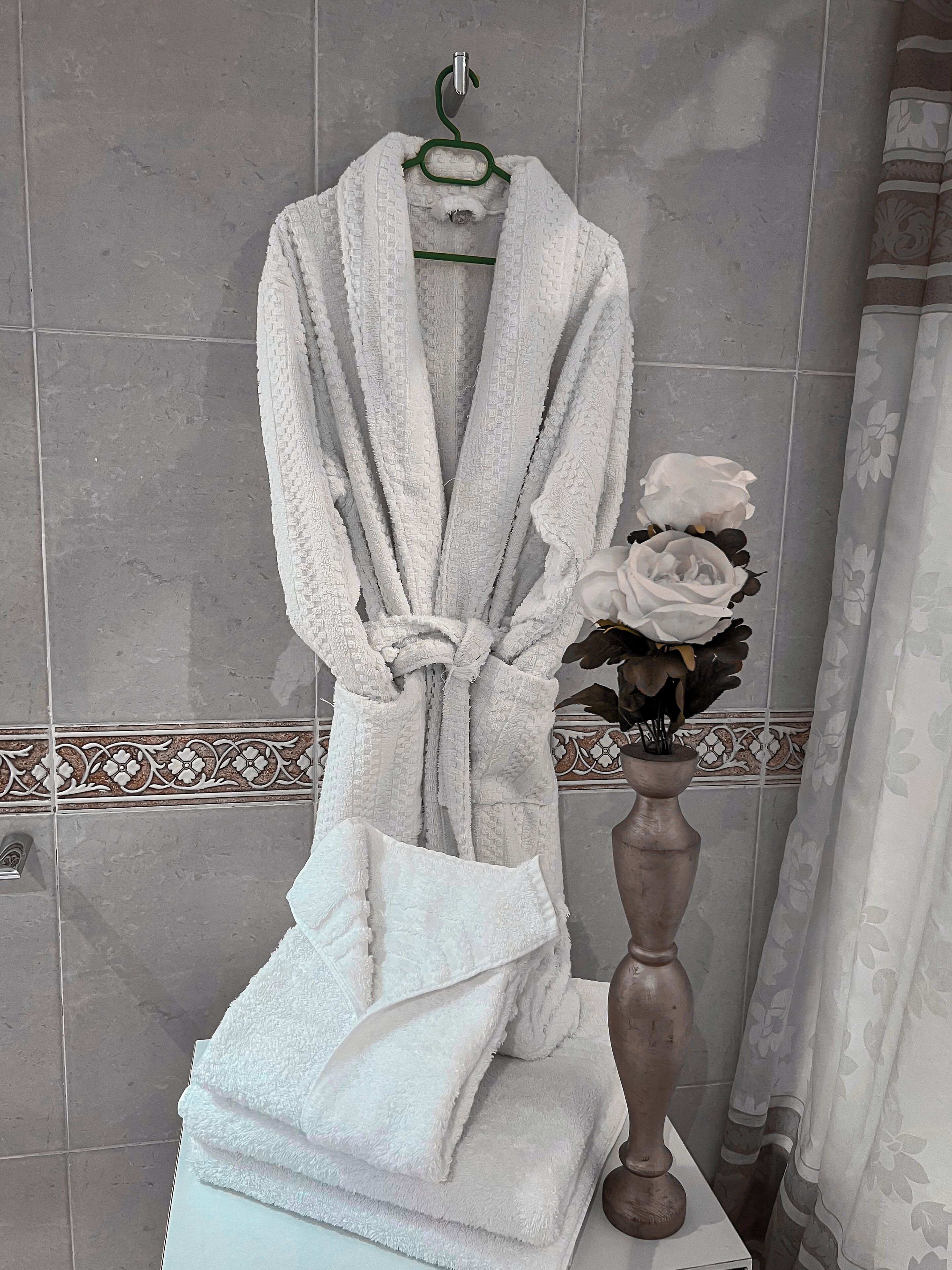 A bathroom with a towel rack holding a white bathrobe, a vase with white flowers, and a decorative tile border.