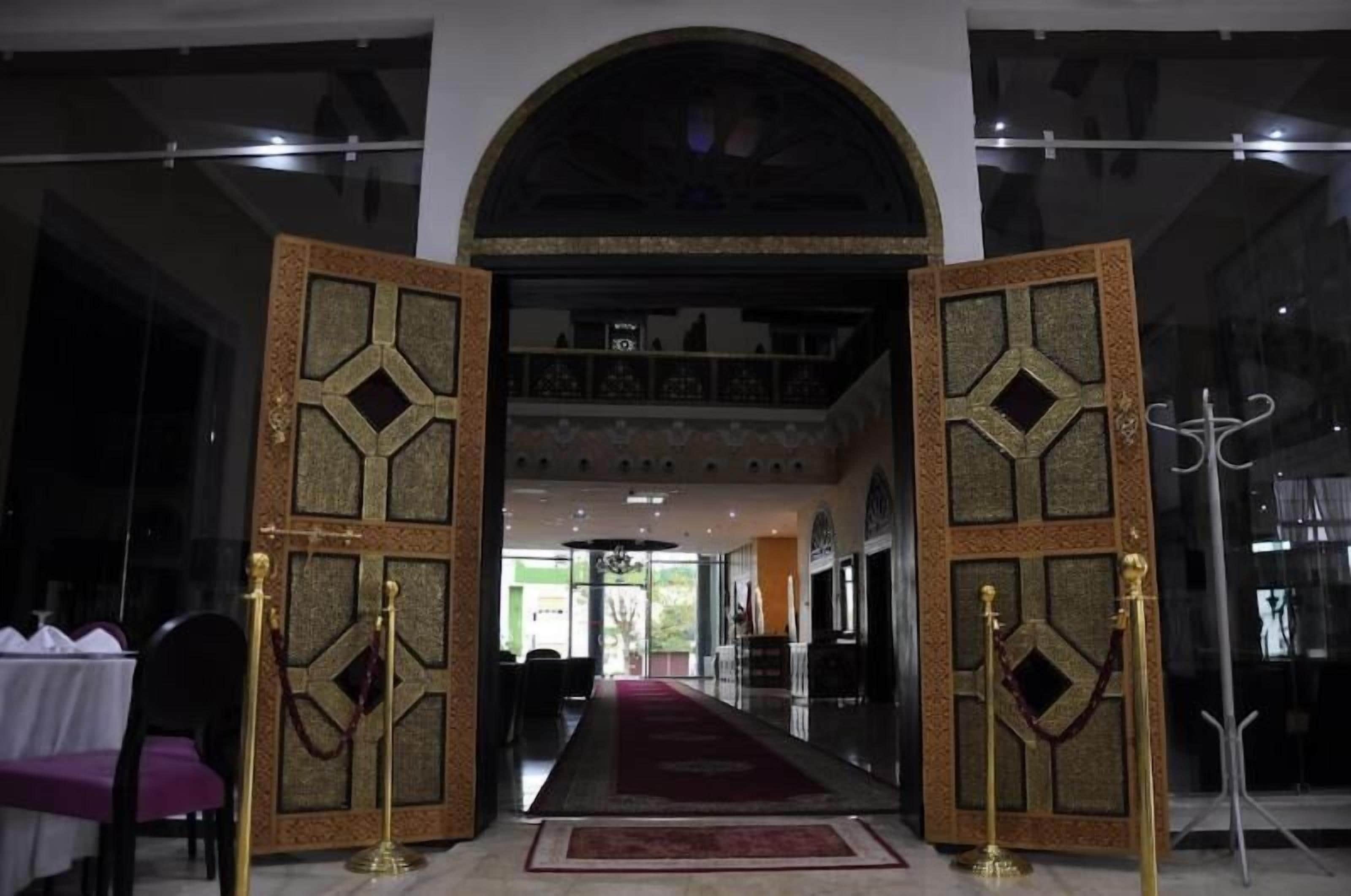 A grand entrance with an arched doorway, a red carpet, and a balcony with a railing.