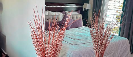 Hotellihuone, jossa on sänky, yöpöytä, koristeellisilla oksilla koristeltu maljakko ja seinällä oleva kukka-aiheinen taulu.