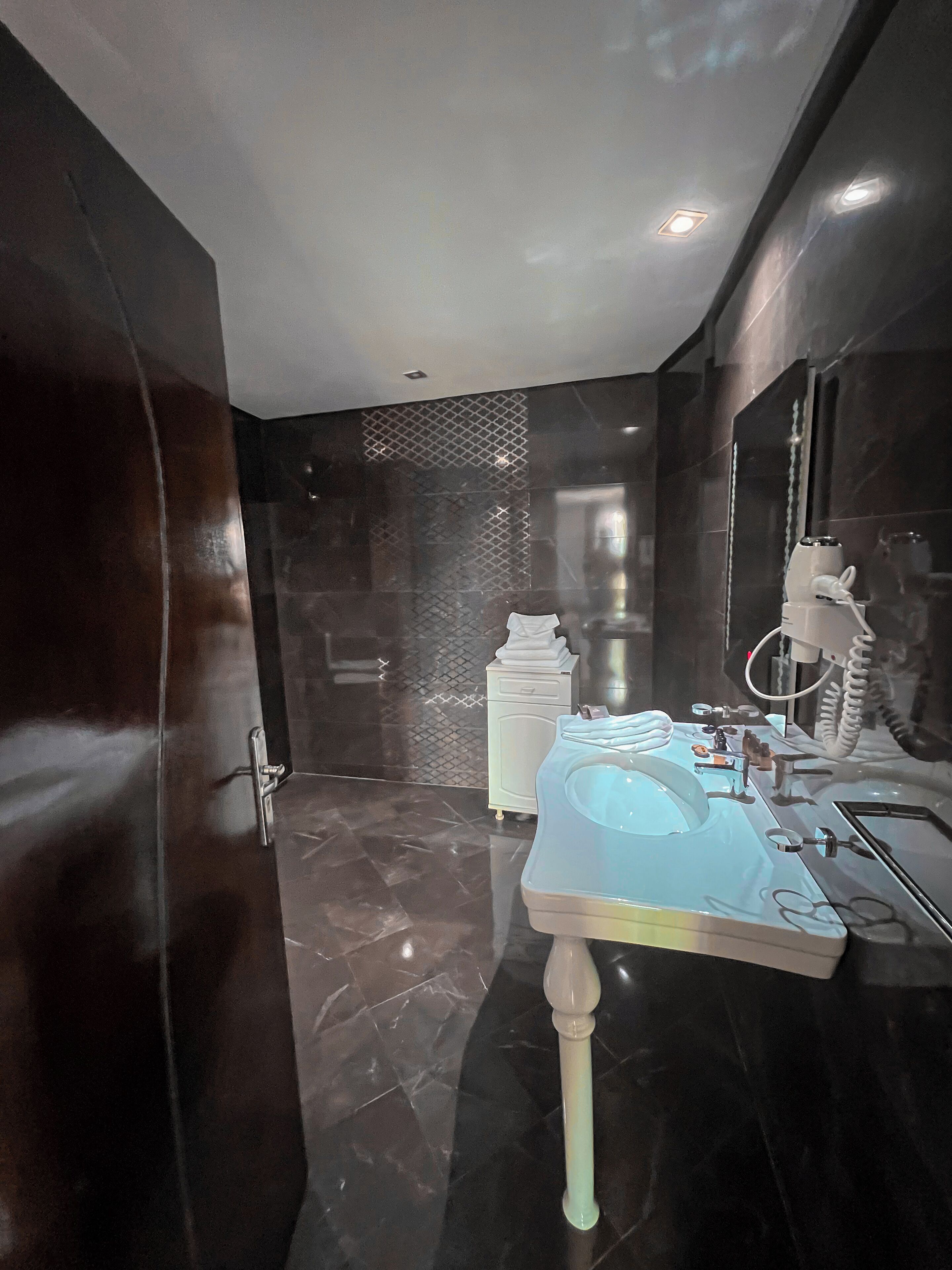 Ein modernes Badezimmer mit dunklem Marmorboden, einem weißen Waschbecken mit blauer Schüssel und einem Spiegel mit Handtuchhalter.