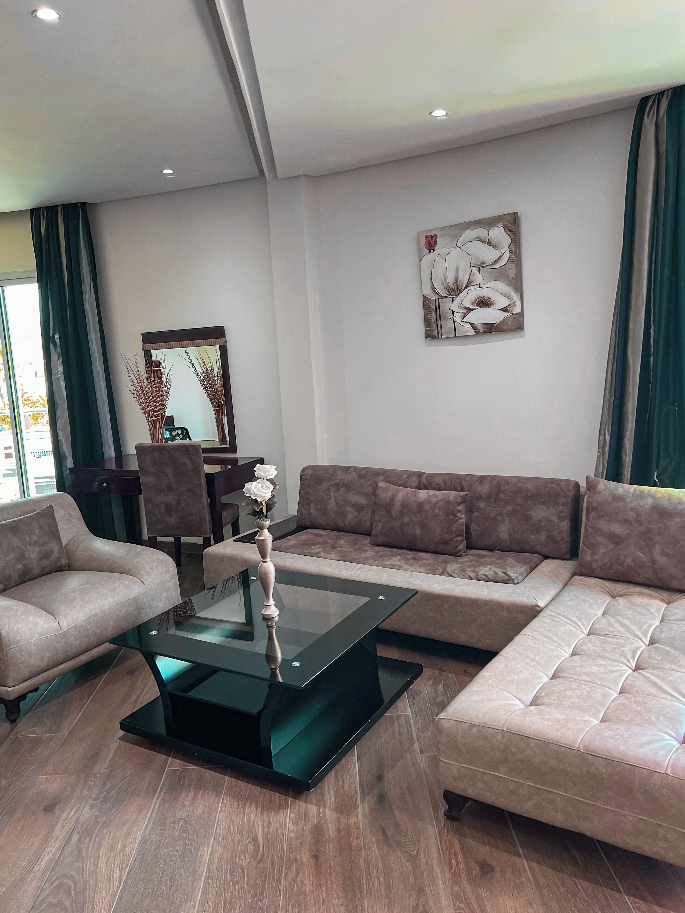 Un salon moderne avec un canapé d’angle, une table basse en verre et un tableau accroché au mur.