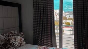 A bedroom with a bed, a headboard, curtains, and a view of the city through a window.