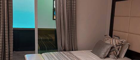 A hotel room with a bed, a bench, and a view of the sky through a window.