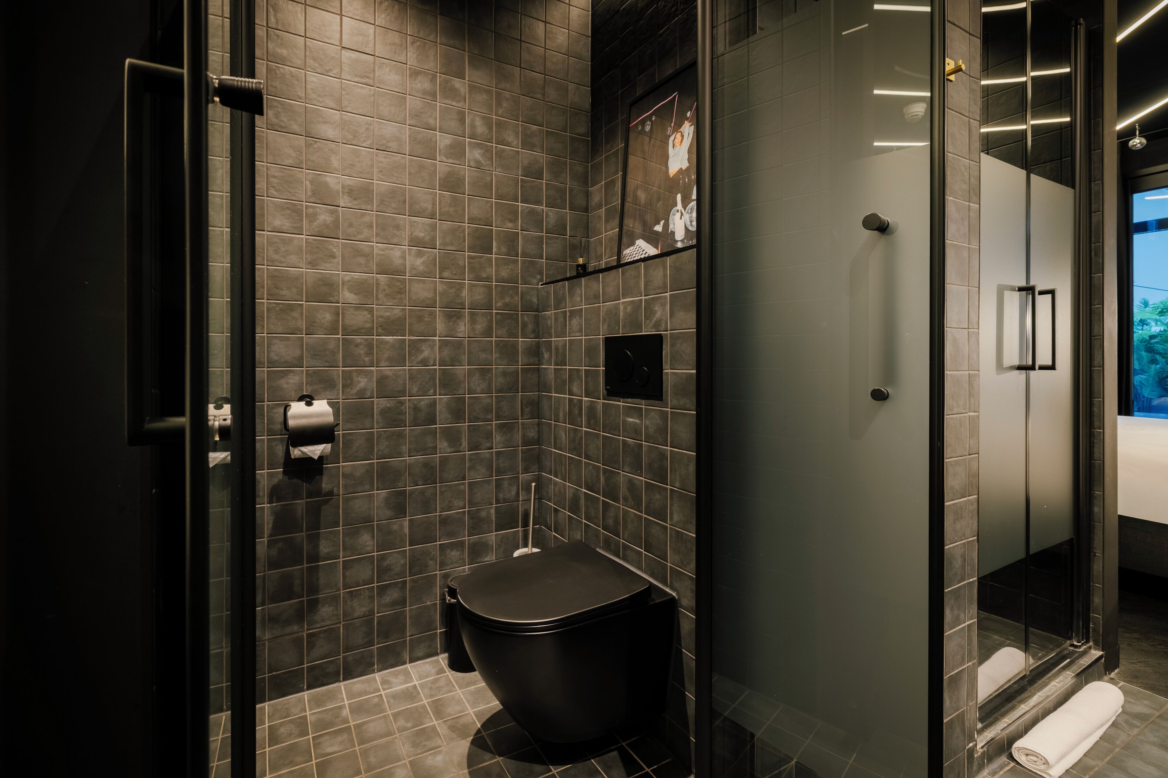 A modern bathroom with a black toilet, a glass shower enclosure, and a tiled wall.