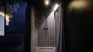 Un petit espace de douche, carrelé, avec une pomme de douche visible et un drain.